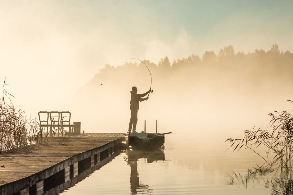 Angler wirft bei Sonnenaufgang an einem ruhigen See seine Kunstködermontage vom Ufer – angeln auf forellen