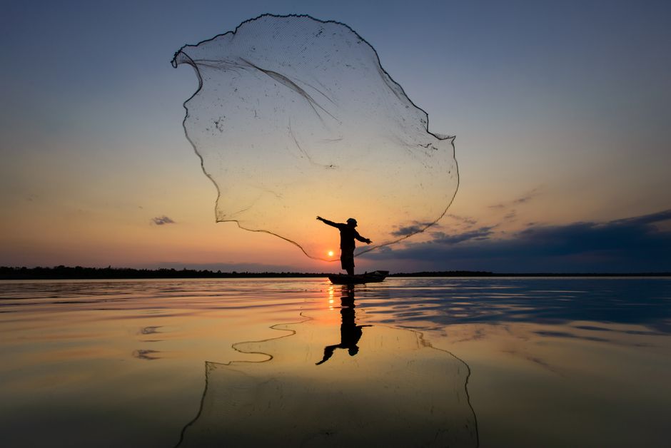 Angler wirft seinen Köder bei Sonnenaufgang vom Boot auf einem ruhigen See – barsch angeln im sommer.