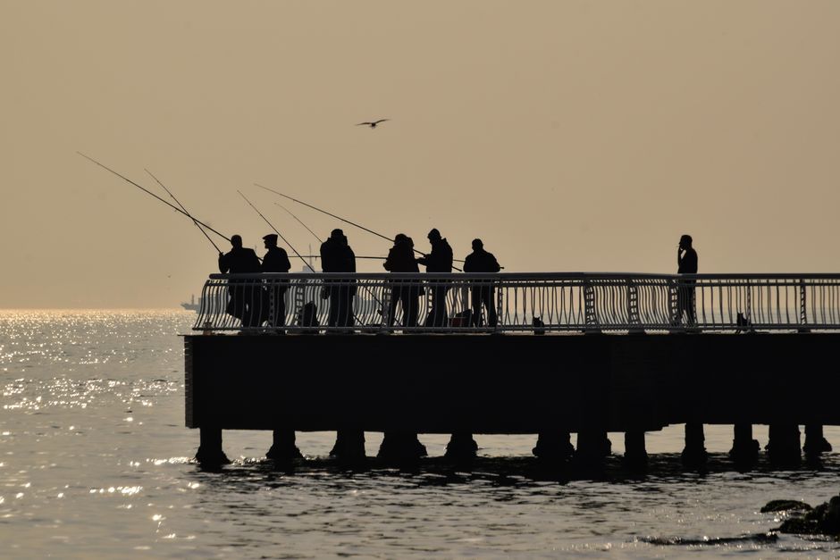 Angler wirft von einer Mole bei Sonnenuntergang einen Metallköder ins Meer – makrelen angeln ostsee